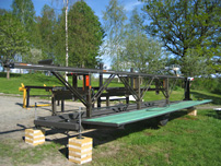 Sågverket i sommarskrud, när det just blivit färdigt. Landgången på sidan är uppfällbar för att hela anläggningen smidigt ska kunna flyttas med traktor.